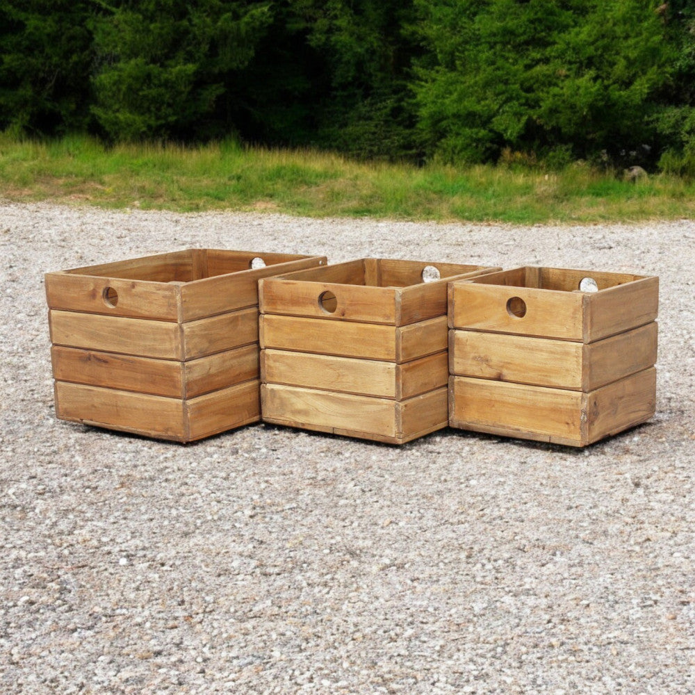 I tre contenitori in legno posizionati all'aperto su ghiaia, evidenziando la resistenza del materiale.