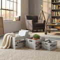 Set di 3 cassette in legno grigio Séline disposte su un tappeto chiaro, contenenti riviste, un plaid e una pianta.
