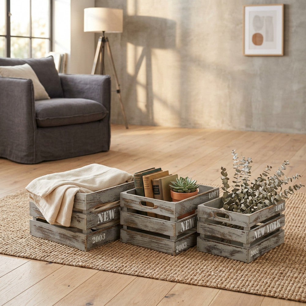 Dettaglio delle cassette in legno Théa utilizzate come contenitori per coperte, libri e piante, appoggiate su un tappeto in juta in un salotto elegante.