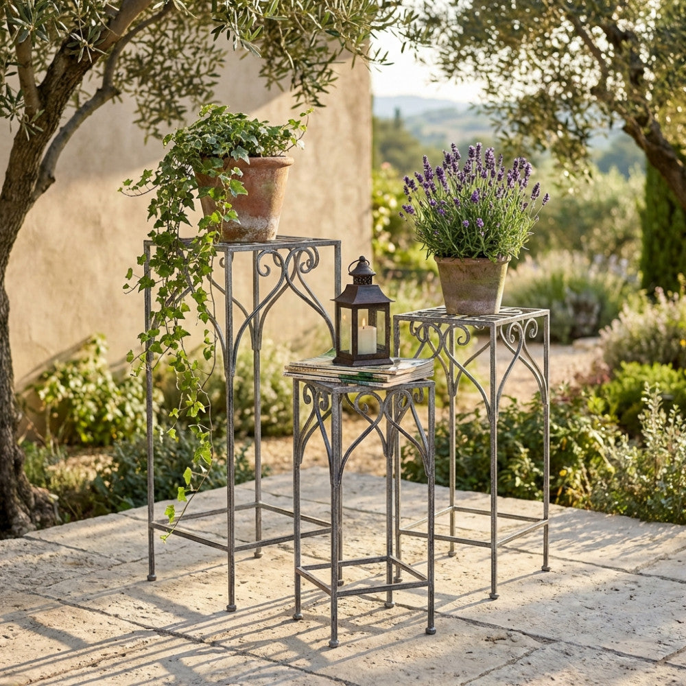 Set di 3 fioriere Vincent in acciaio bianco ossidato disposte all'aperto su un patio in pietra, adornate con edera a cascata, lavanda e una lanterna decorativa.