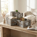 Set di 4 cassette in legno grigio Valérie disposte su un tavolo rustico, utilizzate per contenere coperte e libri in un salotto luminoso.