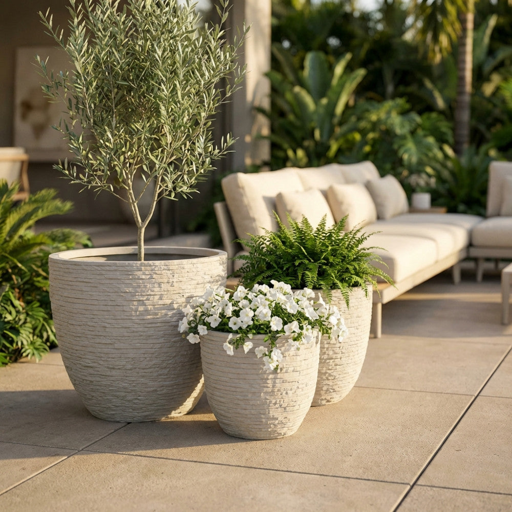 Vasi da esterno in fibra di argilla beige contenenti piante verdi e fiori bianchi, posizionati accanto a un divano lounge in un patio lussuoso.