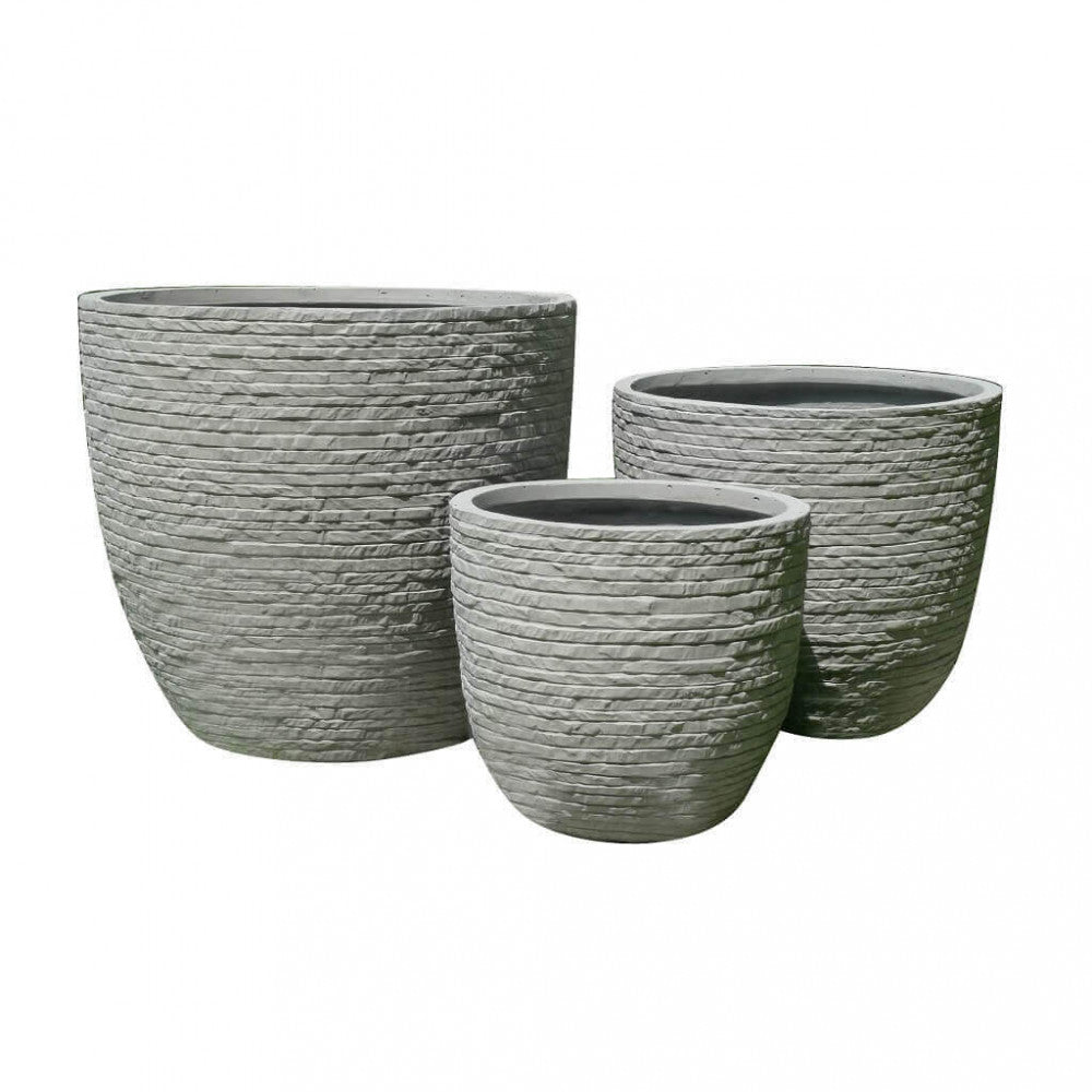 Scatto in studio di tre vasi Ciclamino vuoti in fibra di argilla, che evidenzia la texture materica a rilievo e i volumi scalari su sfondo bianco.