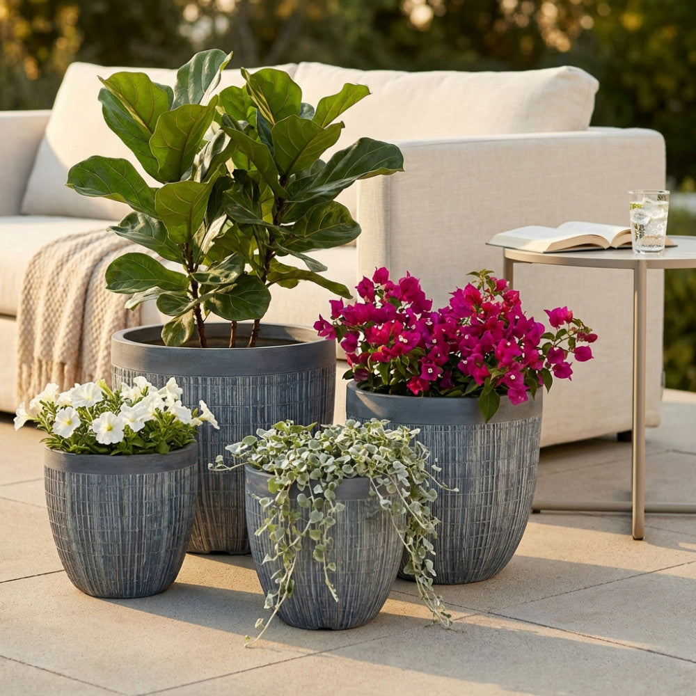 Set di quattro vasi Garofano in fibra sintetica grigia, disposti su un patio soleggiato e arricchiti con piante verdi e fiori vivaci.