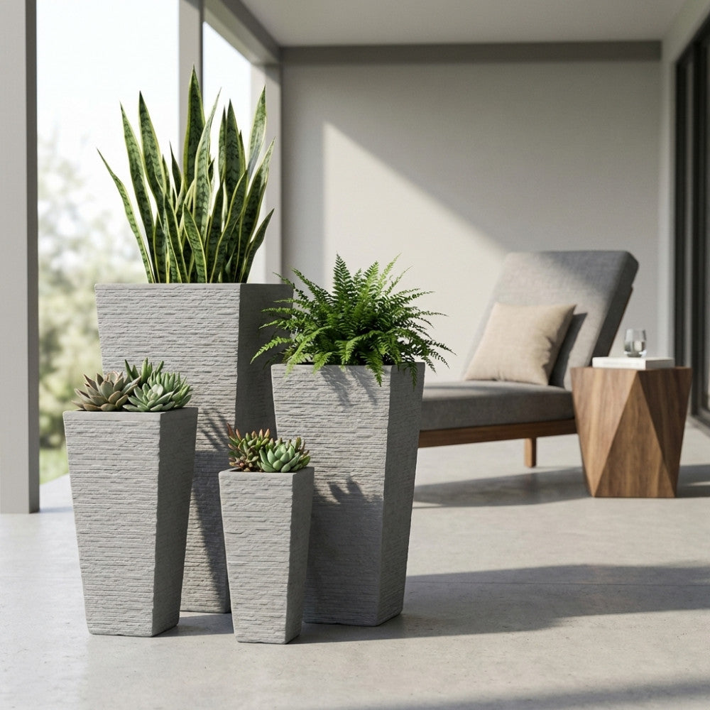 Set di quattro vasi Giglio in fibra di argilla grigia disposti su un patio moderno, arricchiti con piante verdi ornamentali.
