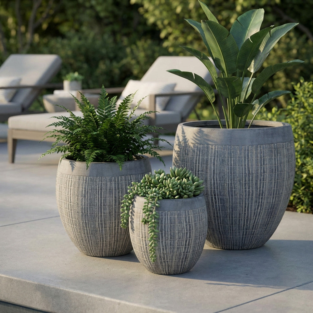 Set di tre vasi Ginepro in fibra sintetica grigia con piante decorative su un patio moderno.