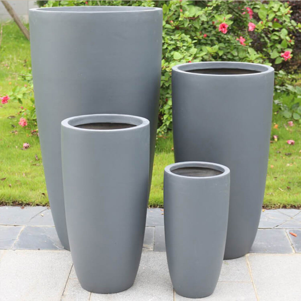 I quattro vasi in fibra di argilla grigia posizionati in un giardino verdeggiante, evidenziando la loro integrazione armoniosa con l'ambiente naturale.