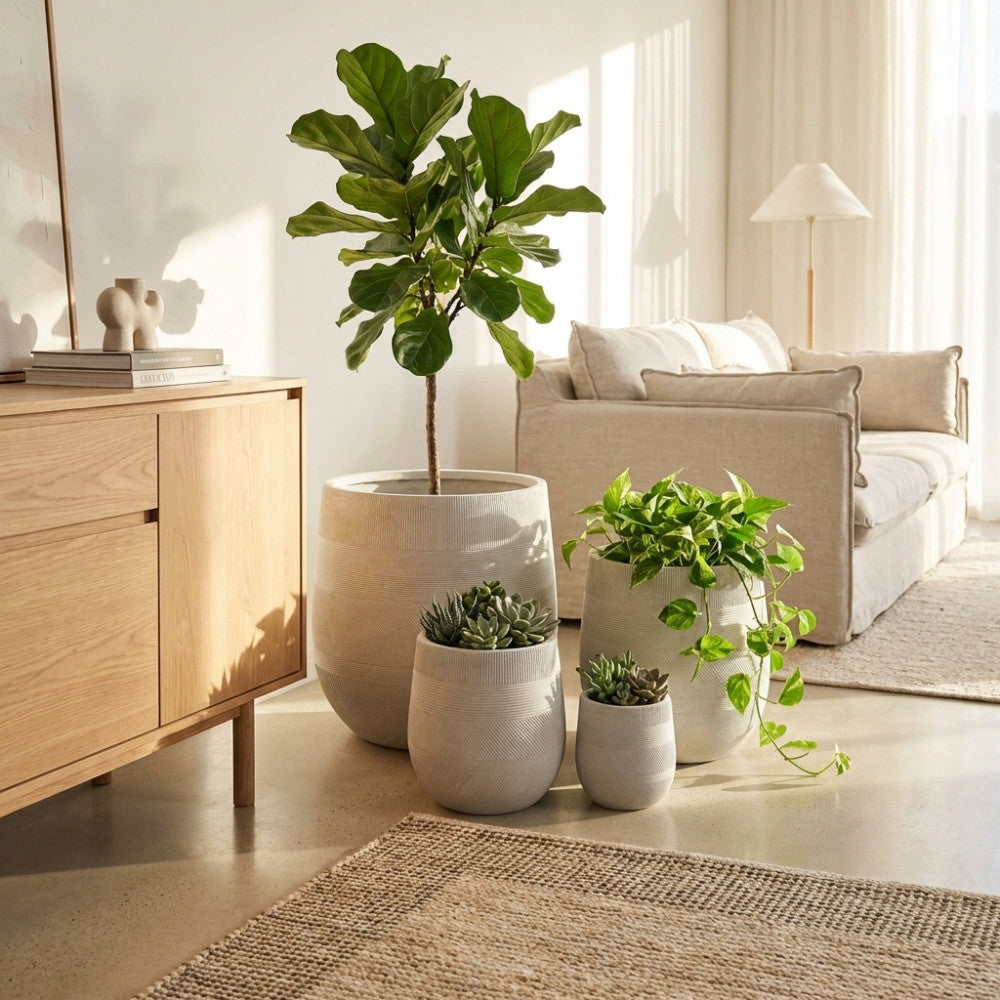 Set di quattro vasi Peonia in fibra sintetica beige disposti in un luminoso soggiorno minimalista, affiancati a una consolle in legno e un divano in tessuto chiaro.
