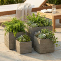 Set di quattro vasi quadrati marroni in fibra sintetica con texture scanalata, allestiti su un patio in pietra con piante grasse e felci.