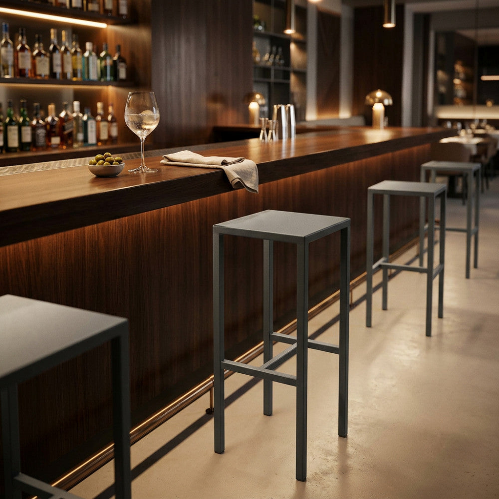 Serie di sgabelli moderni in metallo allineati lungo un bancone bar in legno scuro.