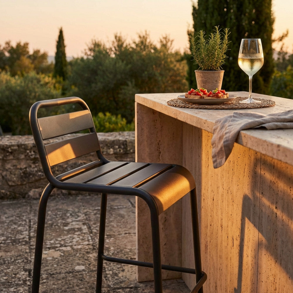 Dettaglio dello sgabello alto Vega illuminato dalla luce calda del tramonto in un elegante giardino mediterraneo.