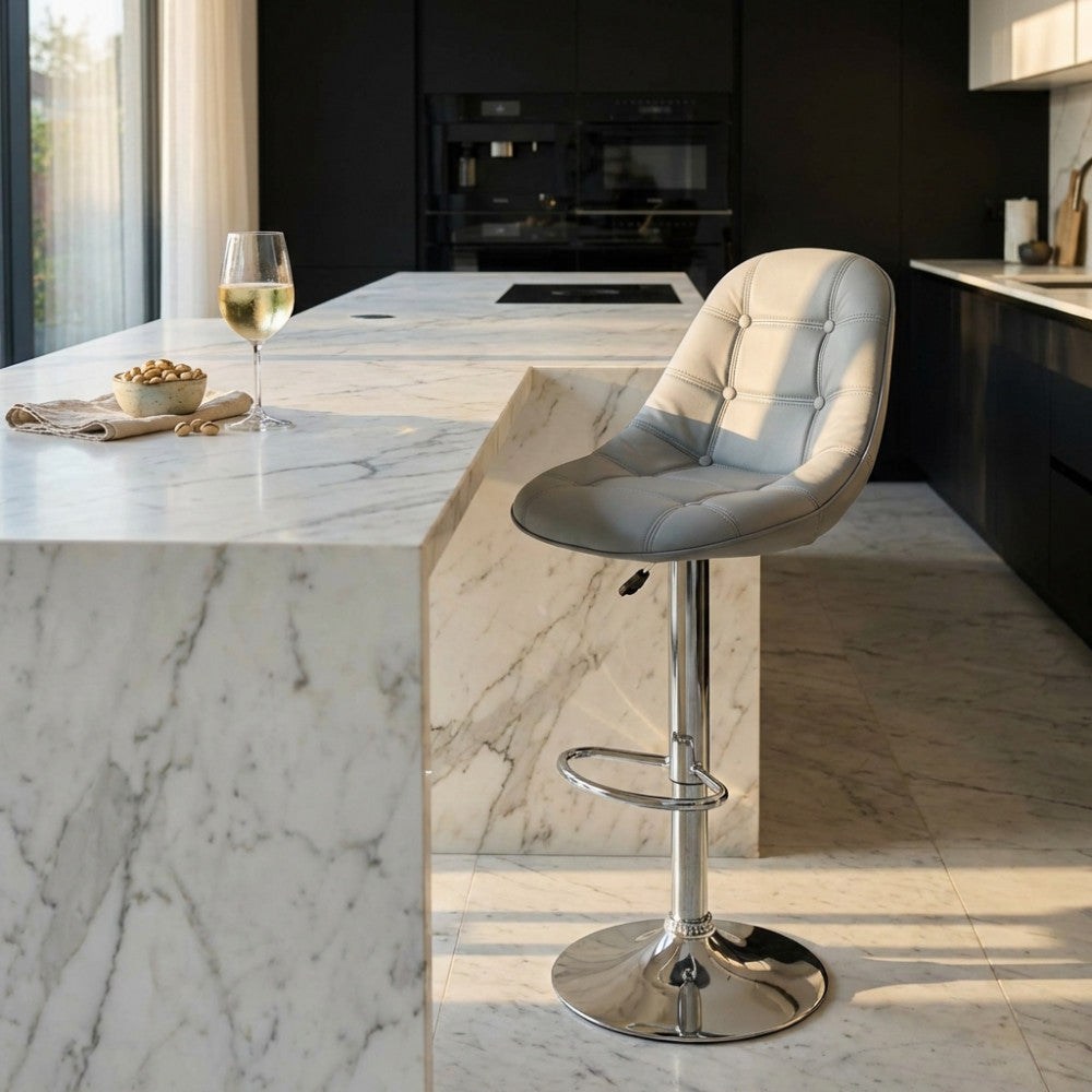 Sgabello Flynn grigio in ecopelle posizionato accanto a un'isola cucina in marmo bianco illuminata dalla luce naturale.