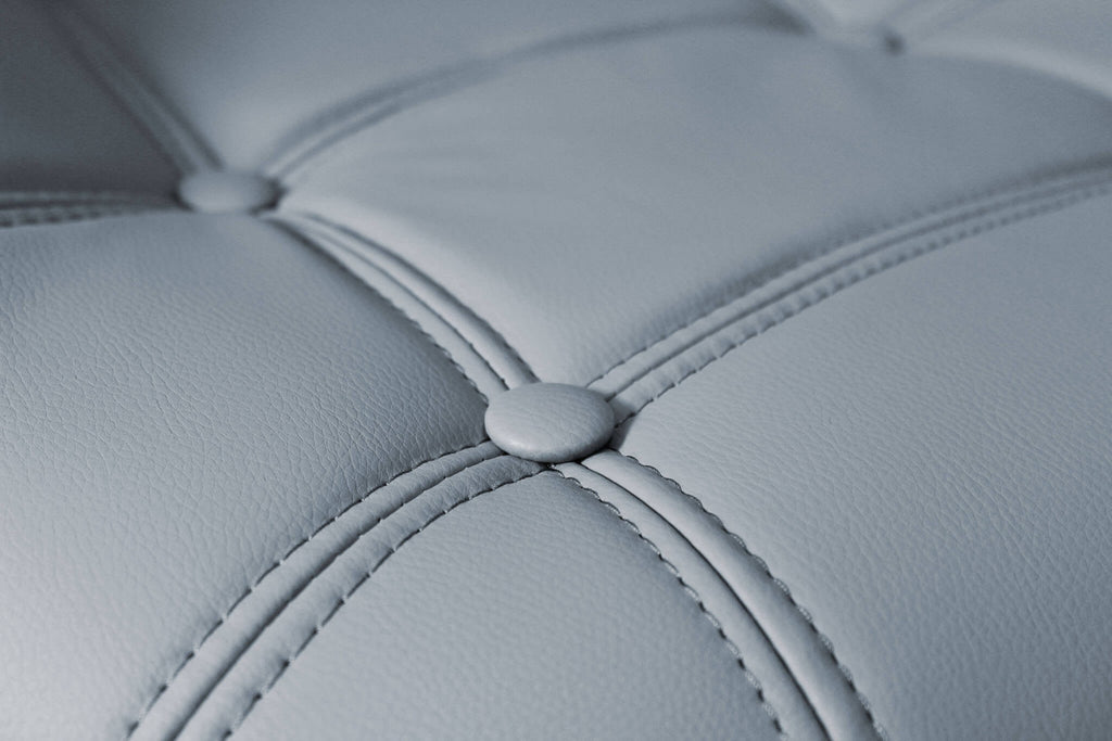 Primo piano della texture in ecopelle grigia dello sgabello Flynn, che mostra le cuciture sartoriali e i bottoni decorativi.