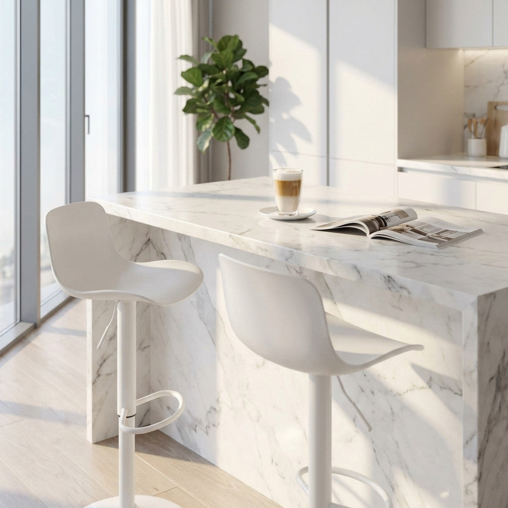 Sgabello Innsbruck in plastica bianca posizionato accanto a un'elegante isola cucina in marmo illuminata dalla luce naturale.