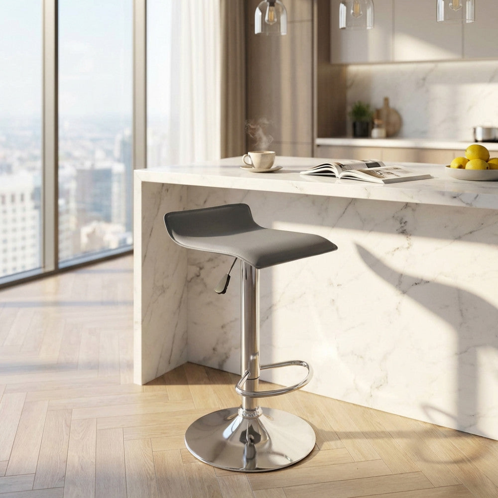 Sgabello Jake in ecopelle grigio chiaro posizionato accanto a un'isola cucina in marmo bianco illuminata dalla luce naturale.