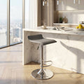 Sgabello Jake in ecopelle grigio chiaro posizionato accanto a un'isola cucina in marmo bianco illuminata dalla luce naturale.