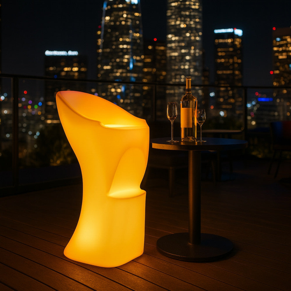 Un singolo sgabello luminoso Scorpius accanto a un elegante tavolino nero da cocktail su una terrazza panoramica con lo skyline della città di notte.