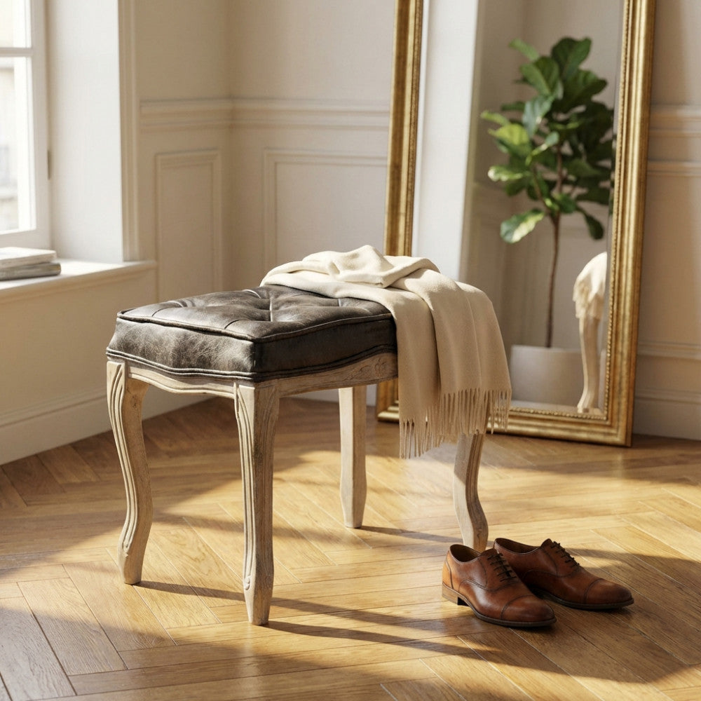 Sgabello Marly in ecopelle vintage grigia e legno posizionato in un salotto luminoso con specchio dorato e pianta decorativa.