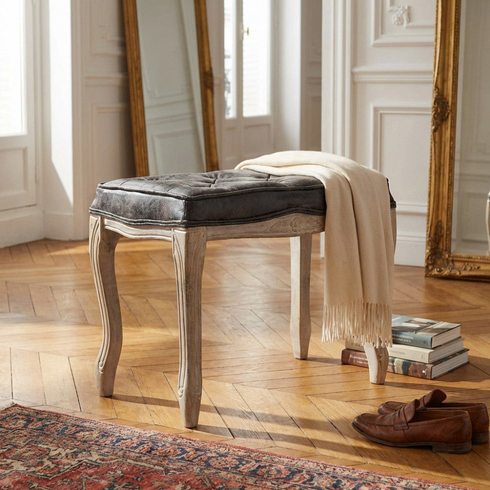 Vista laterale dello sgabello classico Marly con un morbido plaid in cashmere appoggiato sulla seduta capitonné e scarpe in pelle.