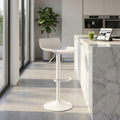 Sgabello Merano bianco dal design moderno posizionato accanto a un'isola cucina in marmo illuminata dalla luce naturale.