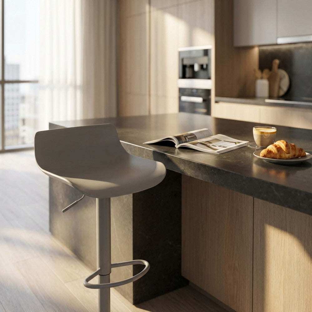 Sgabello moderno grigio inserito in una cucina elegante con penisola scura, affiancato da una colazione con croissant e caffè.