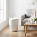 Pouf sgabello Cliff in plastica bianca ambientato in un luminoso soggiorno moderno accanto a un divano grigio.