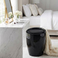 Sgabello pouf Cliff nero lucido posizionato accanto a una toeletta in marmo bianco in una camera da letto luminosa.