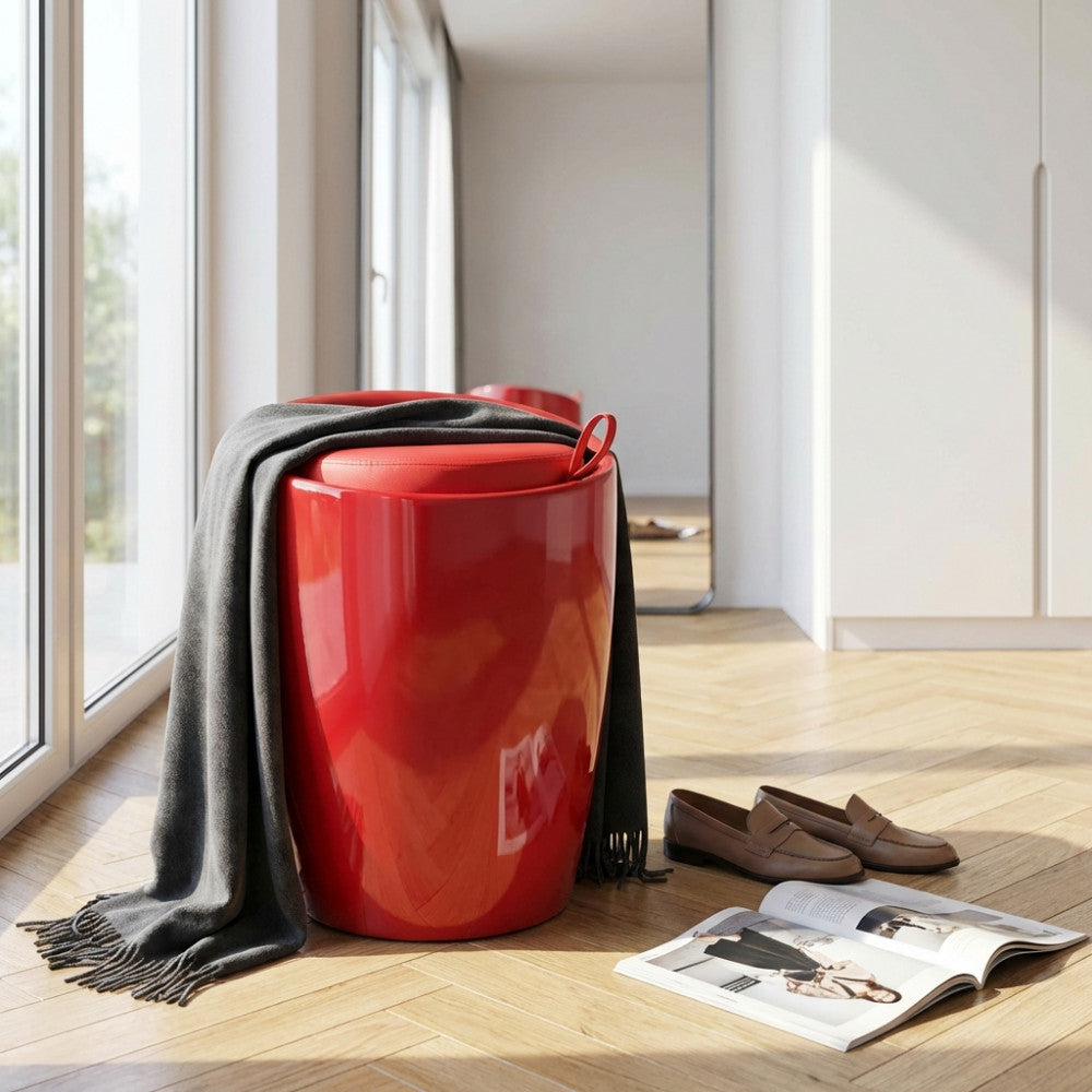 Sgabello pouf rosso lucido con coperta grigia appoggiata, situato in un soggiorno luminoso con pavimento in legno.