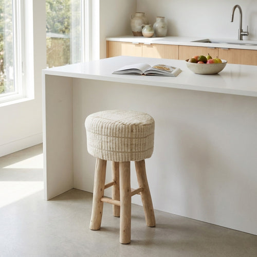 Sgabello nordico Valentin con seduta in cotone e lana di fronte a un bancone cucina bianco.