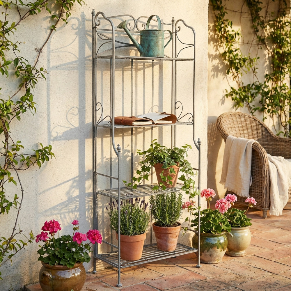 Dettaglio dell'étagère in acciaio posizionata contro un muro intonacato, decorata con edera, lavanda e un annaffiatoio vintage.