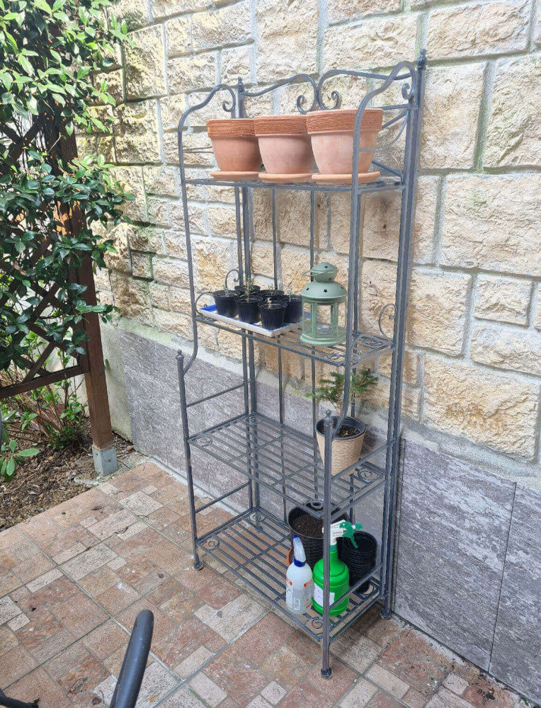 Étagère in acciaio bianco ossidato posizionata all'aperto contro un muro in pietra, utilizzata per organizzare piccole piantine e attrezzi da giardinaggio.