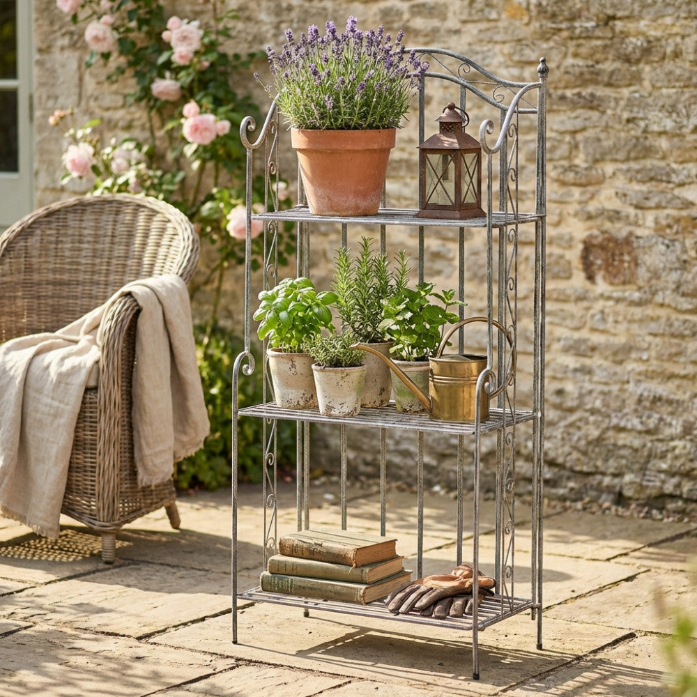 Étagère in acciaio bianco ossidato allestita in un giardino con piante aromatiche, libri e un innaffiatoio in ottone.