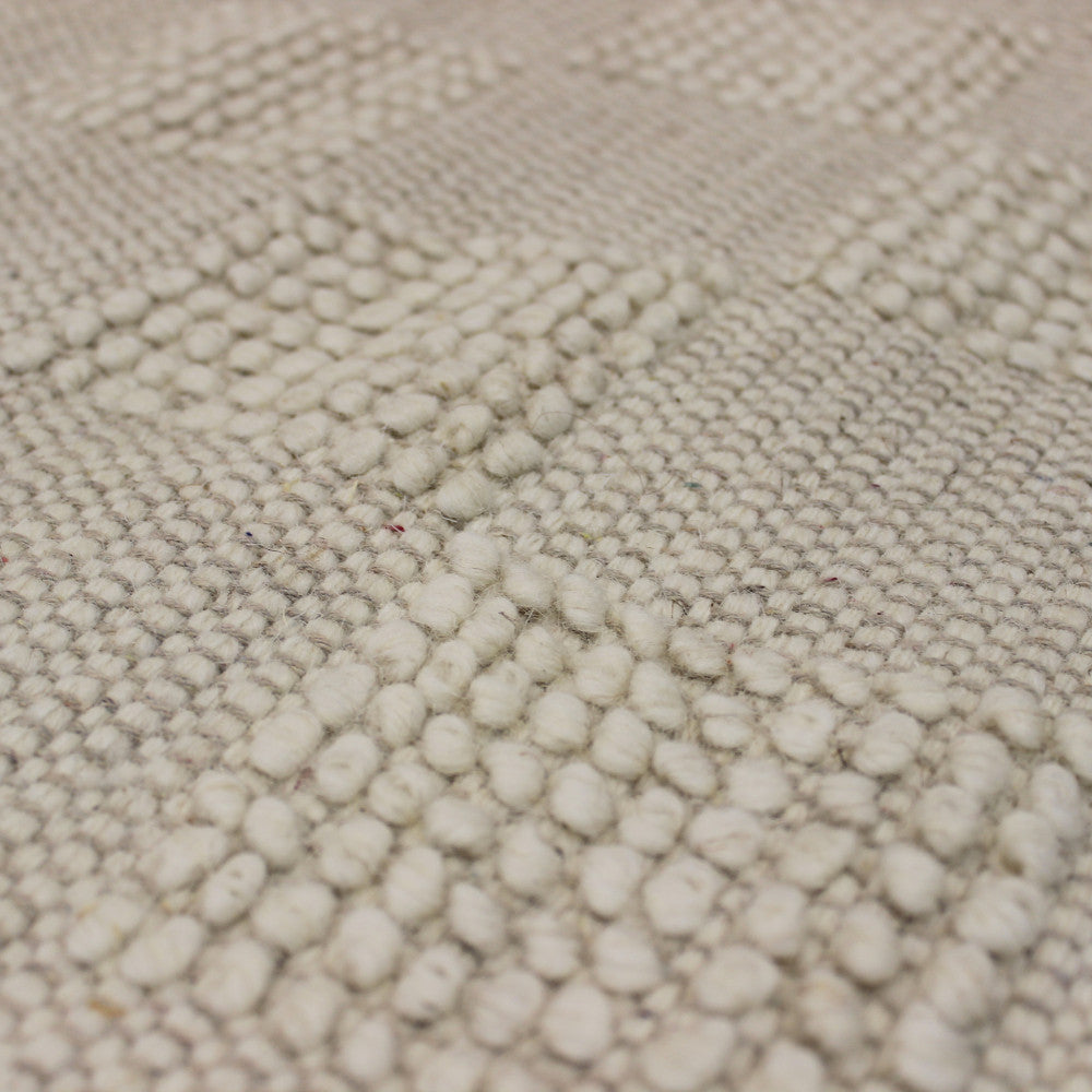 Macro fotografia della superficie tattile del tappeto, mostrando la qualità artigianale dei filati bianco beige.