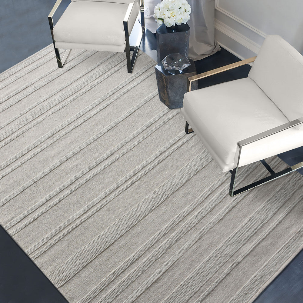 Prospettiva angolata del tappeto Antoine in un ambiente elegante con sedute di design e tavolino scultoreo.