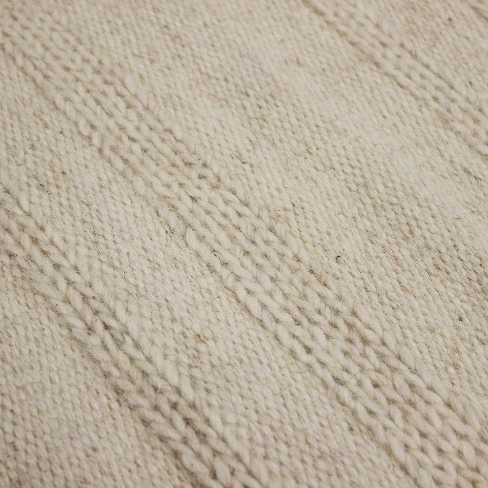 Macro fotografia della texture del tappeto, mostrando l'intreccio robusto dei filati in lana e cotone beige.