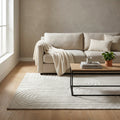 Tappeto Aurélien bianco beige ambientato in un salotto luminoso con divano chiaro e tavolino in legno.