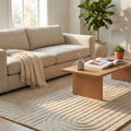 Tappeto moderno Aurélien bianco e beige ambientato in un salotto luminoso con divano chiaro.