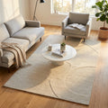 Tappeto moderno Bastien in lana e cotone bianco beige, ambientato in un luminoso soggiorno con divano grigio e tavolino in marmo.
