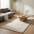 Tappeto moderno Bastien in lana e cotone bianco e beige, posizionato in un salotto luminoso con divano grigio e tavolino in legno.
