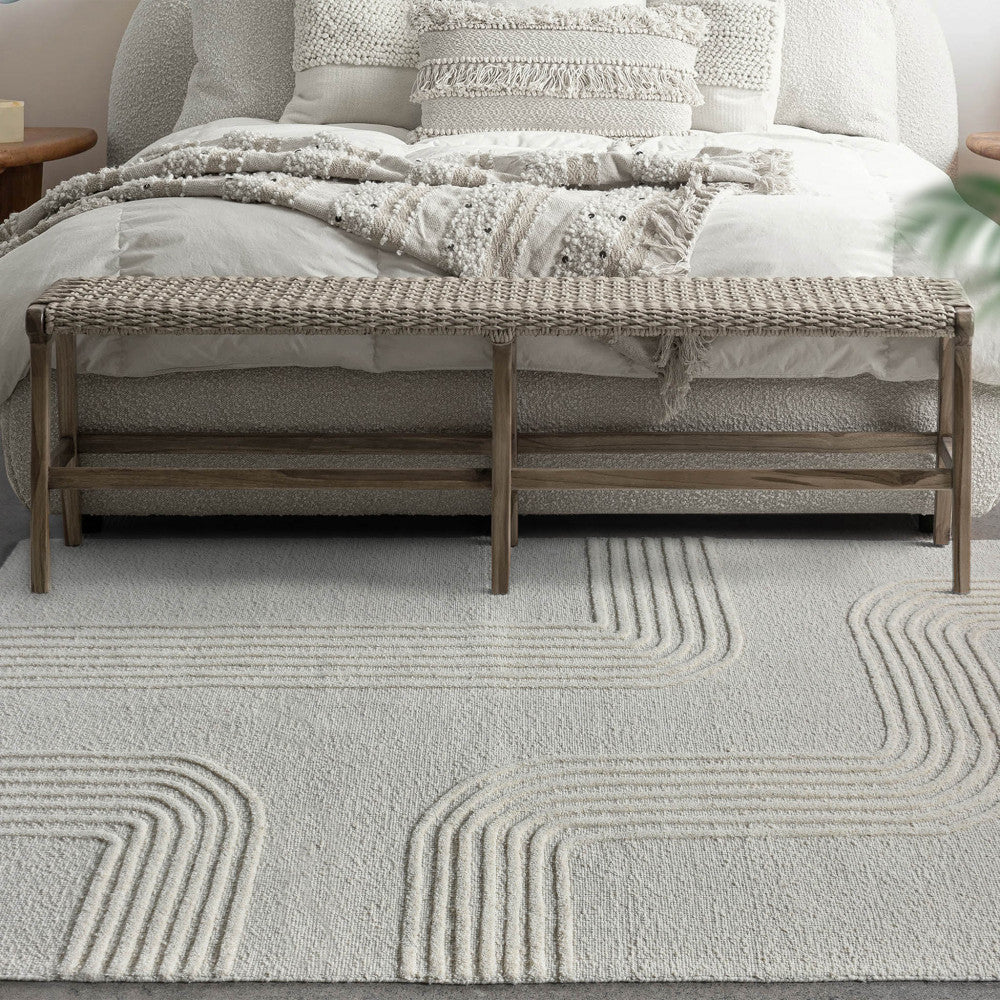 Tappeto Christophe posizionato ai piedi di un letto elegante con panca in legno intrecciato.