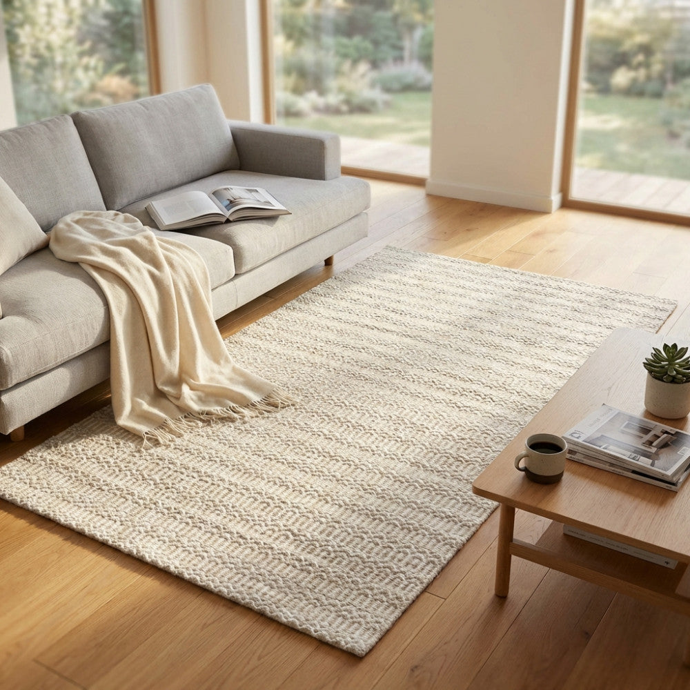 Tappeto moderno Edgard in lana e cotone bianco beige, posizionato in un luminoso soggiorno con divano grigio e pavimento in legno.