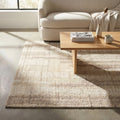 Tappeto moderno Fabien in lana e cotone beige ecrù, posizionato in un soggiorno luminoso sotto un tavolino in legno.