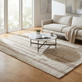 Tappeto moderno Fabien in lana e cotone beige ecrù, posizionato in un luminoso soggiorno con divano bianco e tavolino in marmo.