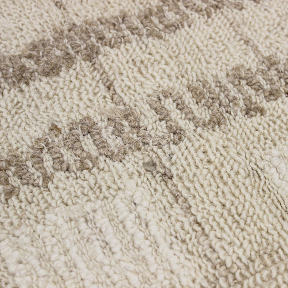 Macro fotografia delle fibre del tappeto Fabien, che mostra la qualità artigianale dei nodi e la morbidezza del filato beige ecrù.