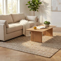 Tappeto Gérard in juta e lana marrone chiaro posizionato in un luminoso soggiorno moderno con divano beige e tavolino in legno.