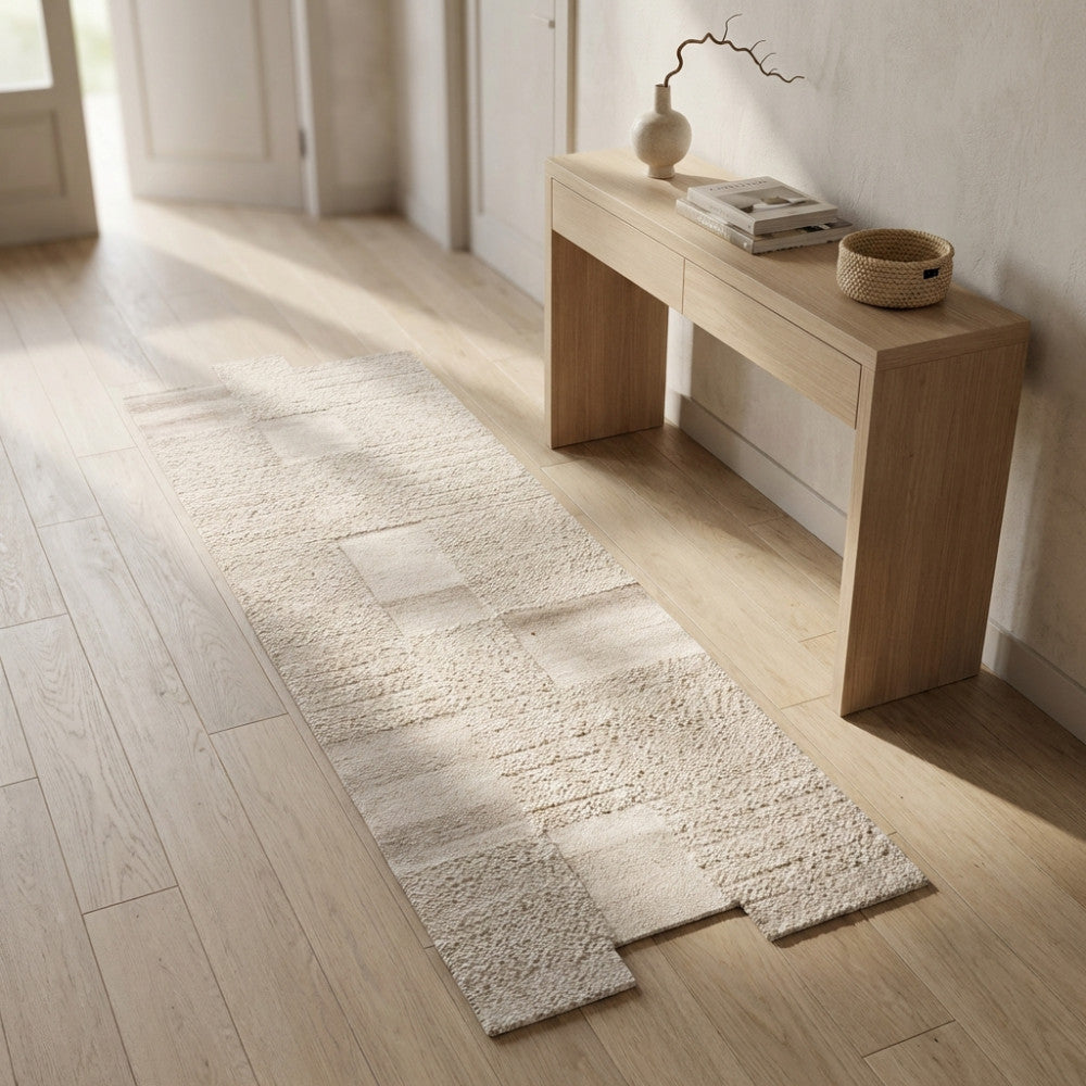 Tappeto Georges beige in lana e poliestere posizionato in un corridoio luminoso accanto a una console in legno.