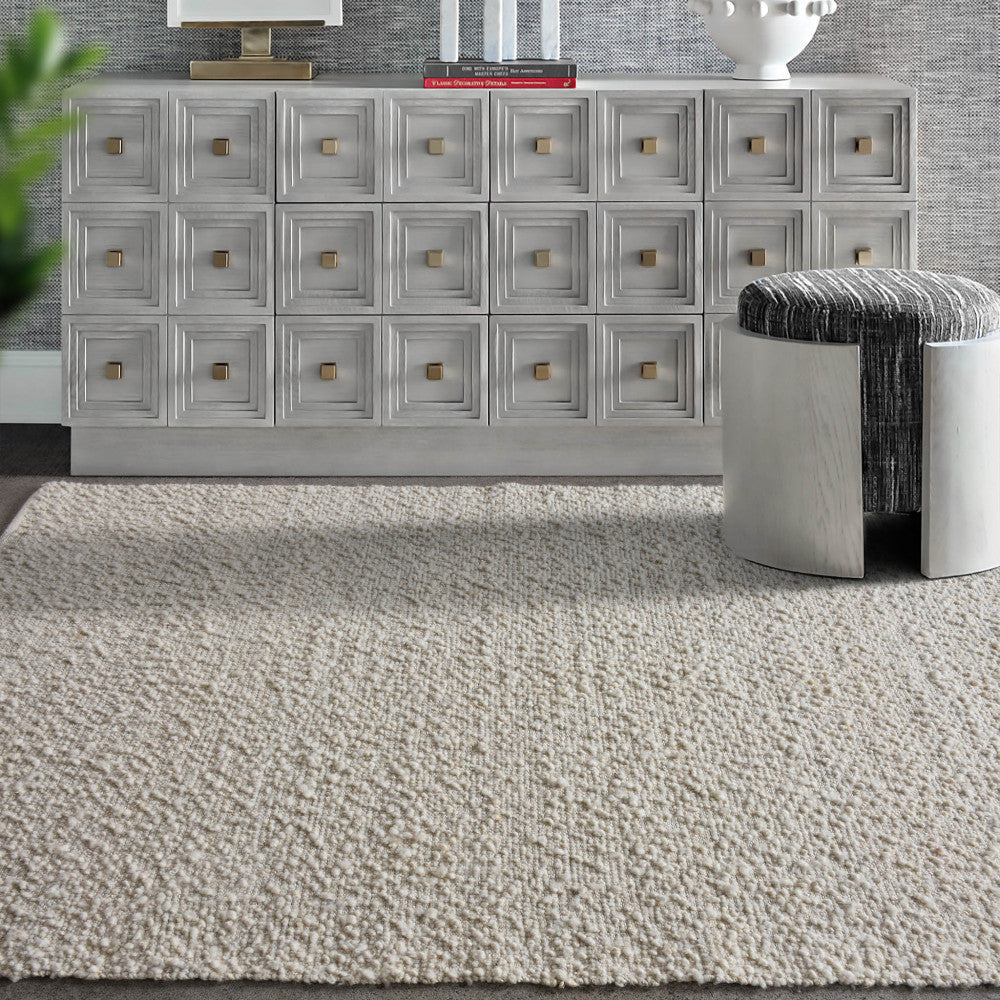Tappeto Hubert in lana e juta ambientato in una zona living elegante con mobile grigio e pouf di design.