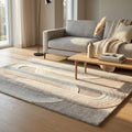 Tappeto moderno beige con motivi geometrici curvi, steso in un luminoso soggiorno con divano grigio chiaro e tavolino in legno.
