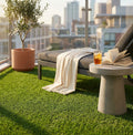Tappeto erboso sintetico in polipropilene verde allestito su un balcone moderno con arredi in cemento e vista panoramica sulla città.
