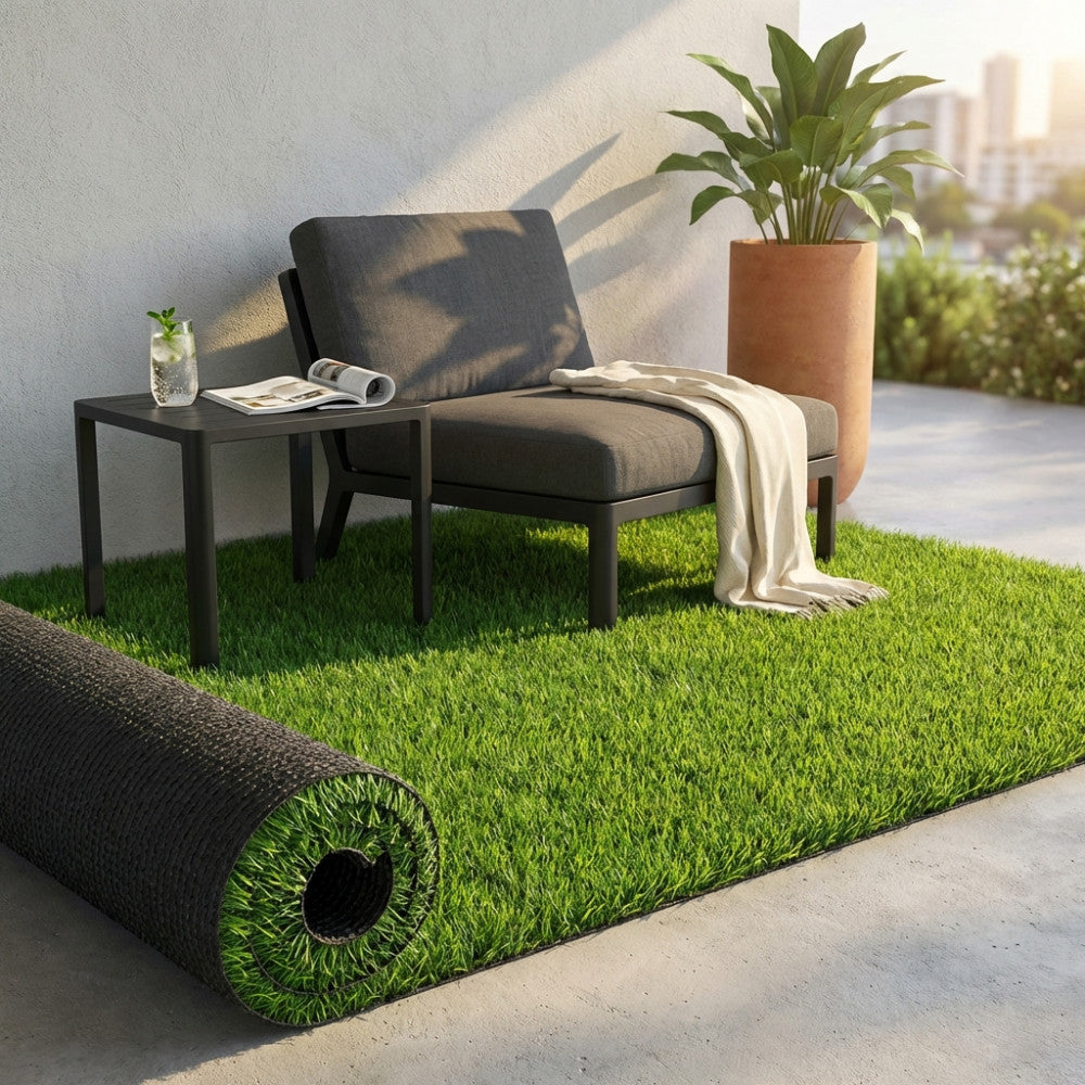 Rotolo di prato artificiale parzialmente srotolato su un terrazzo con seduta lounge scura e piante decorative.